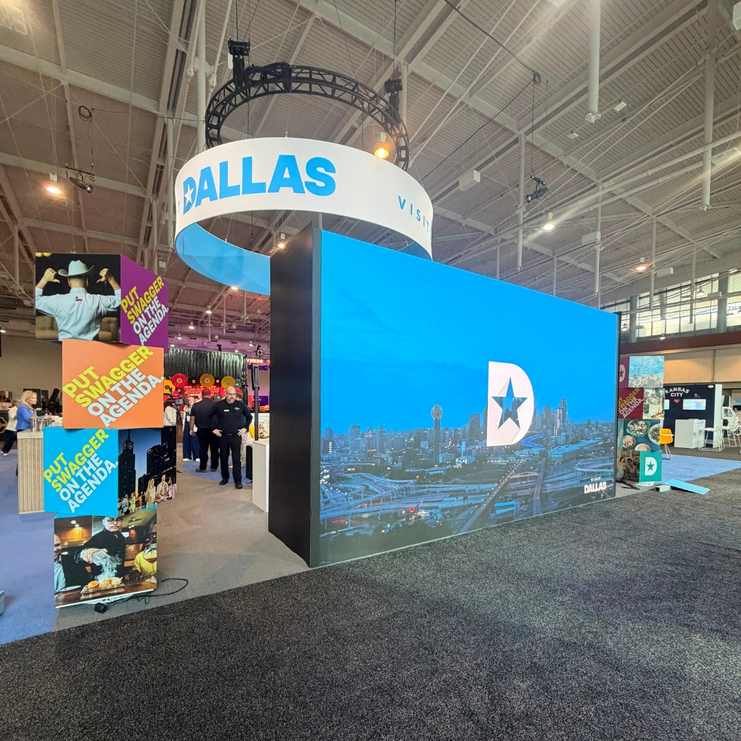 Visit Dallas booth with a large LED wall displaying the Dallas skyline, white touchscreen displays, and branded graphics